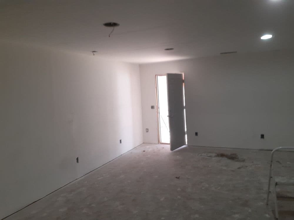 Empty room with white walls, open door, and unfinished flooring. Natural light entering.