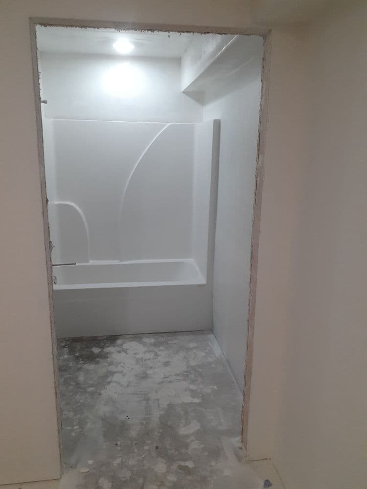 Newly constructed bathroom with a bathtub, white walls, and unfinished flooring.