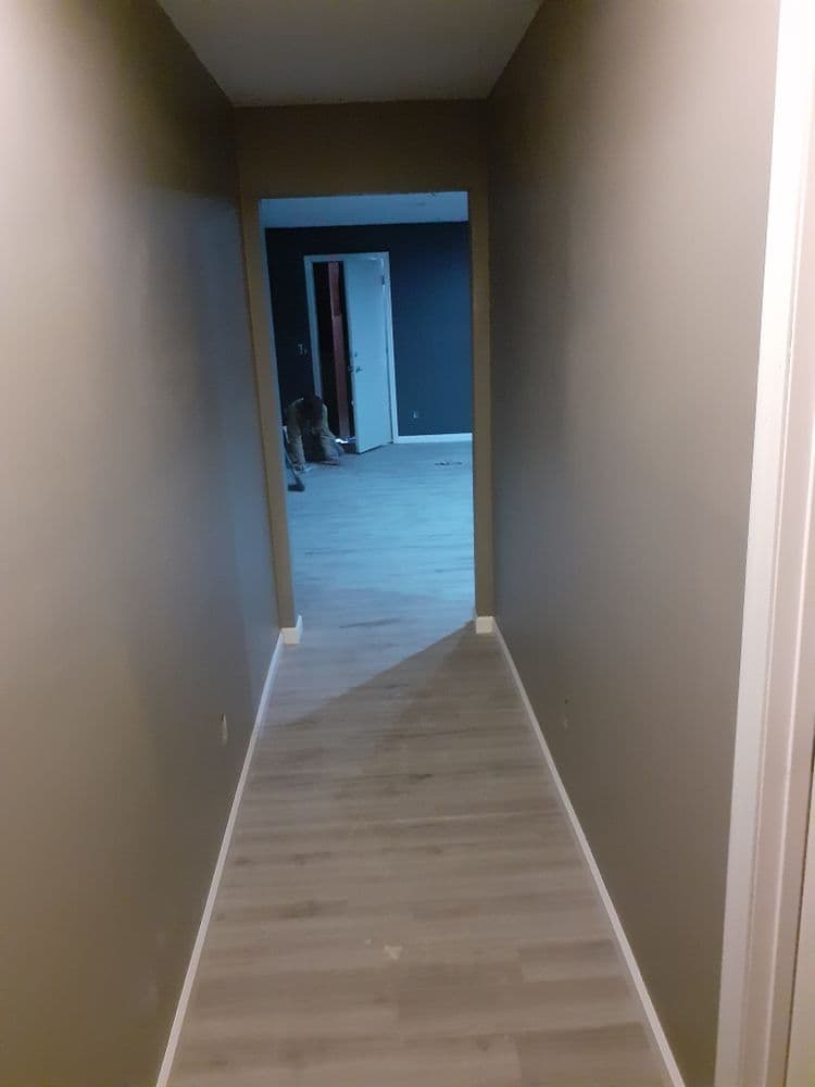 Long hallway with light-colored flooring leading to a doorway and a dark room at the end.
