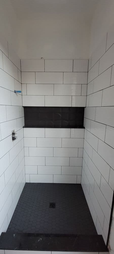 Modern shower stall with white subway tile and dark accent wall featuring hexagon floor tiles.