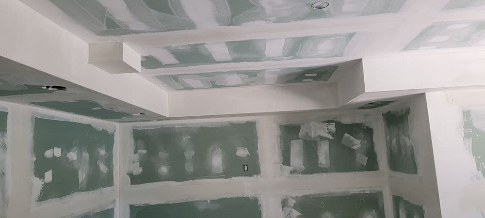 Drywall installation in a room, featuring freshly applied mud and tape on walls and ceiling.