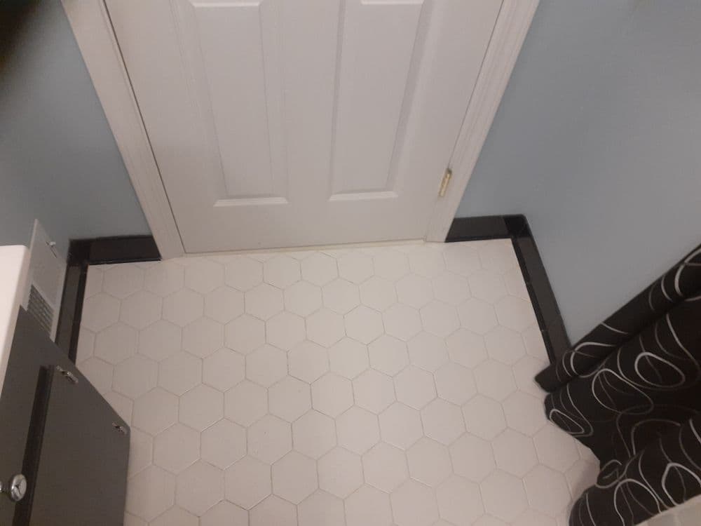 Hexagonal white tile floor with black trim near a closed door and curtain.