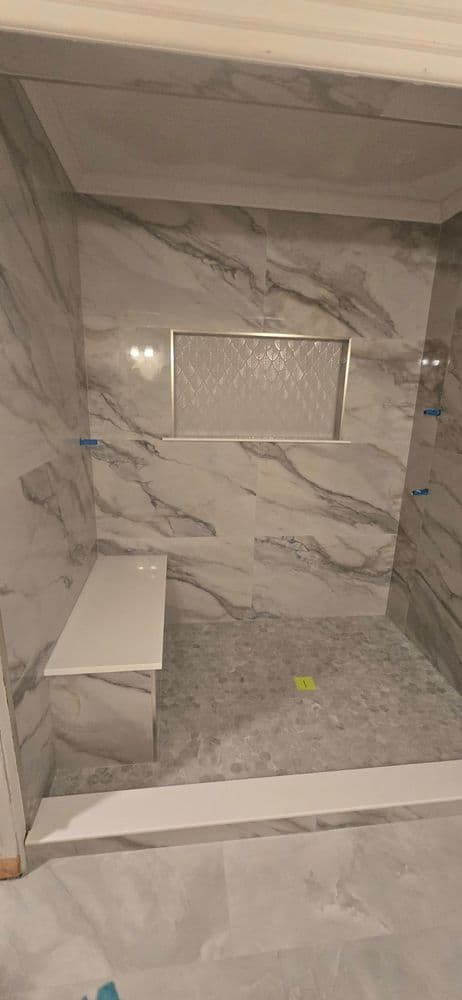 Modern shower with marble walls, built-in bench, and decorative niche for storage.