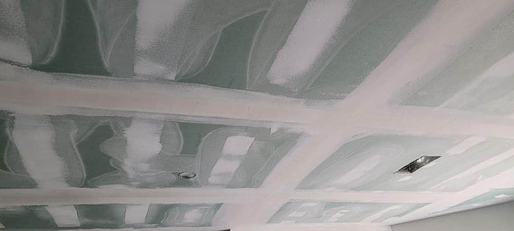 Drywall ceiling with joint compound applied, showing unfinished surface and lighting fixture.