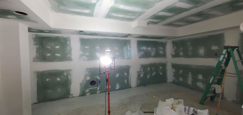 Drywall installation progress in a modern room, with lighting and a ladder in the foreground.