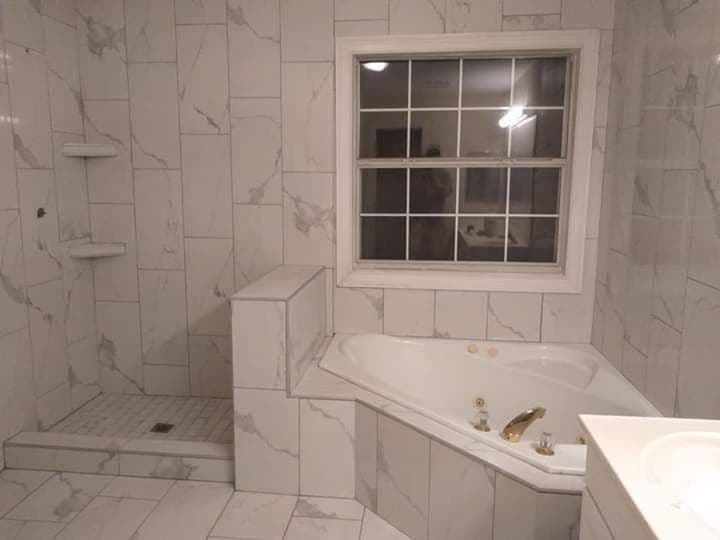 Modern bathroom featuring a marble design, a bathtub, shower, and large window.
