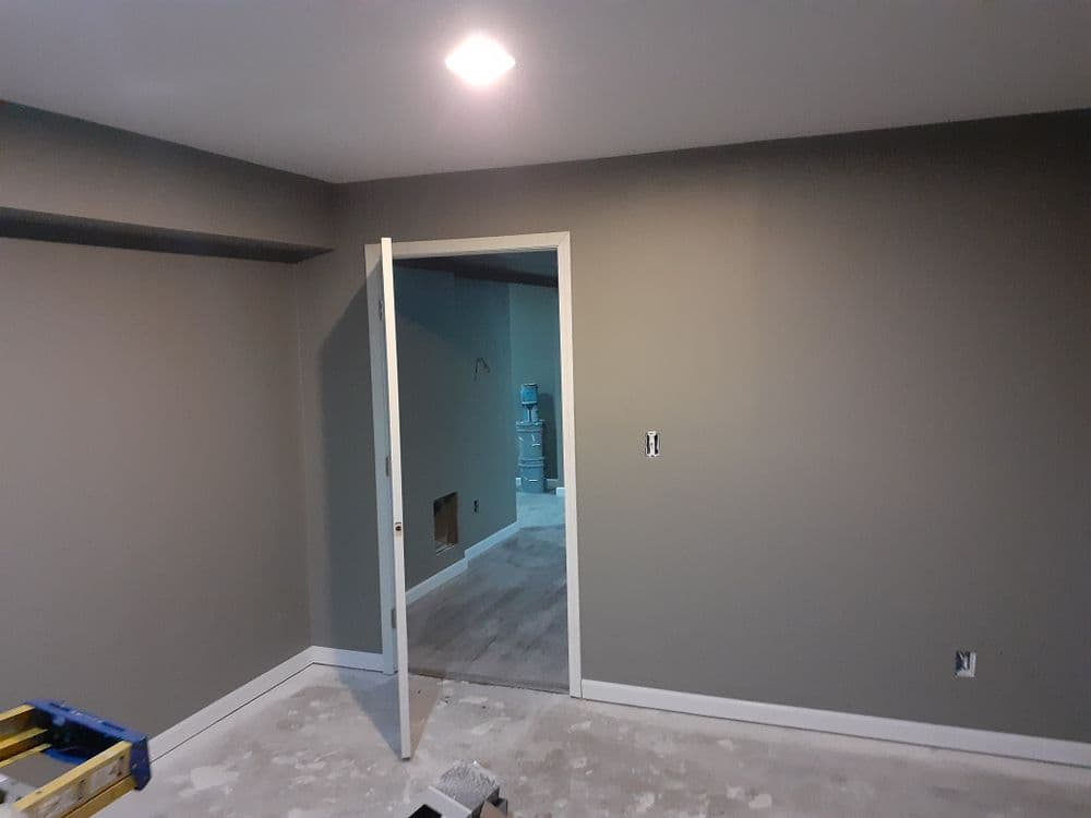 unfinished room with gray walls and open door leading to another space, showing renovation progress