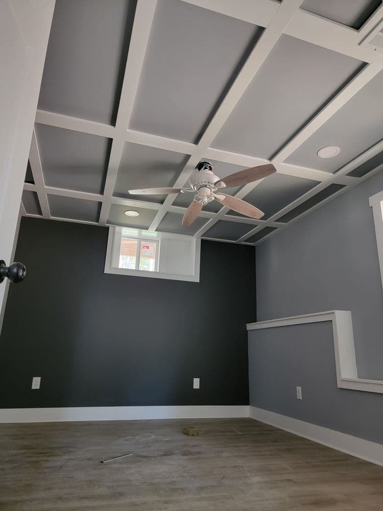 Modern room featuring a coffered ceiling, ceiling fan, and grey walls with wooden flooring.