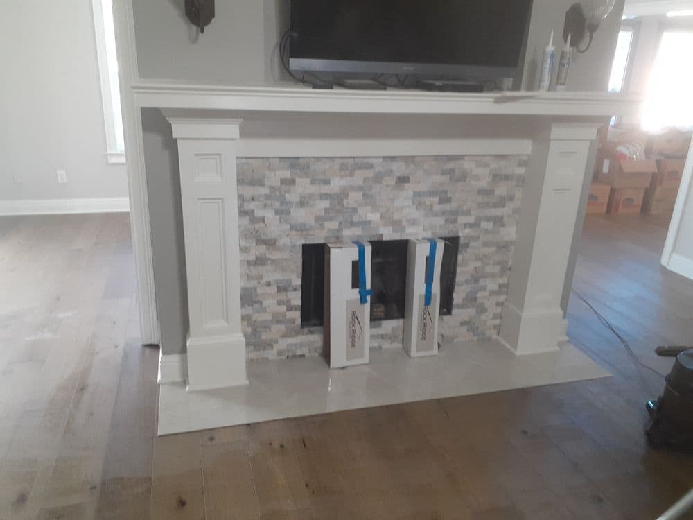 modern fireplace with stone tiles, decorative mantel, and muted grey wood floor in a bright room