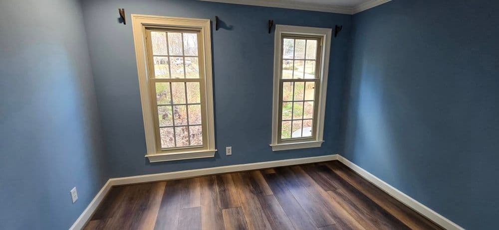 Bright blue room with two windows overlooking a garden, featuring new laminate flooring.