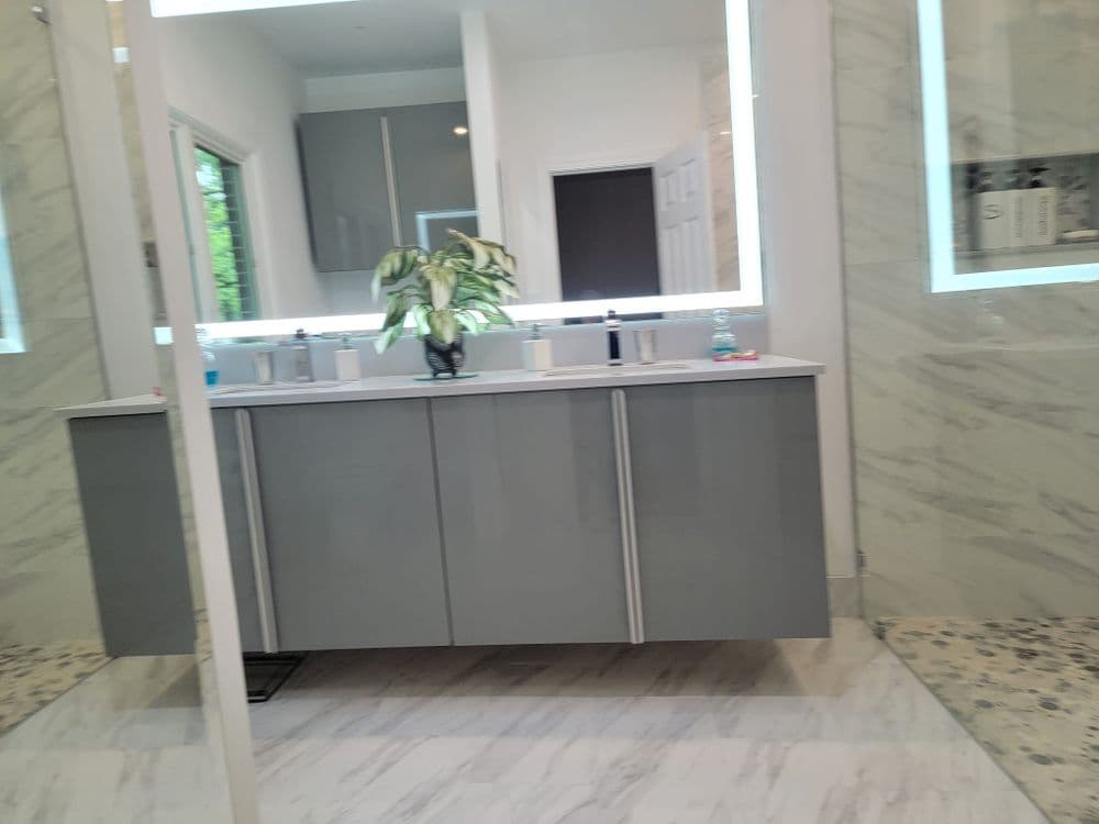 Modern bathroom with gray cabinetry, backlit mirrors, and a potted plant. Elegant marble flooring.
