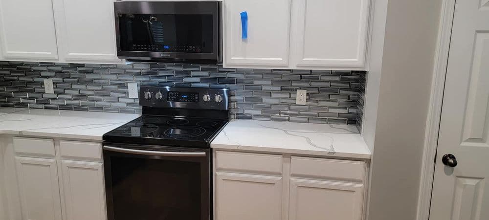 Modern kitchen with stainless steel appliances, marble countertop, and stylish tile backsplash.