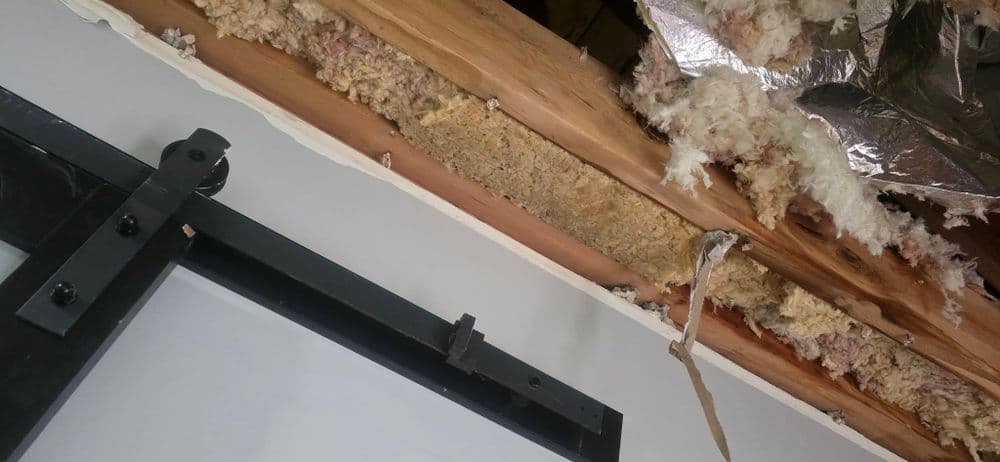 Damaged ceiling insulation exposed with wood beams and metal fixtures visible.