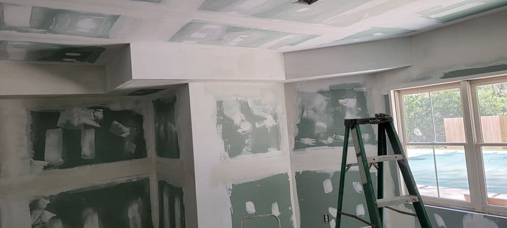 Room undergoing drywall finishing with green taped walls and a ladder in view.
