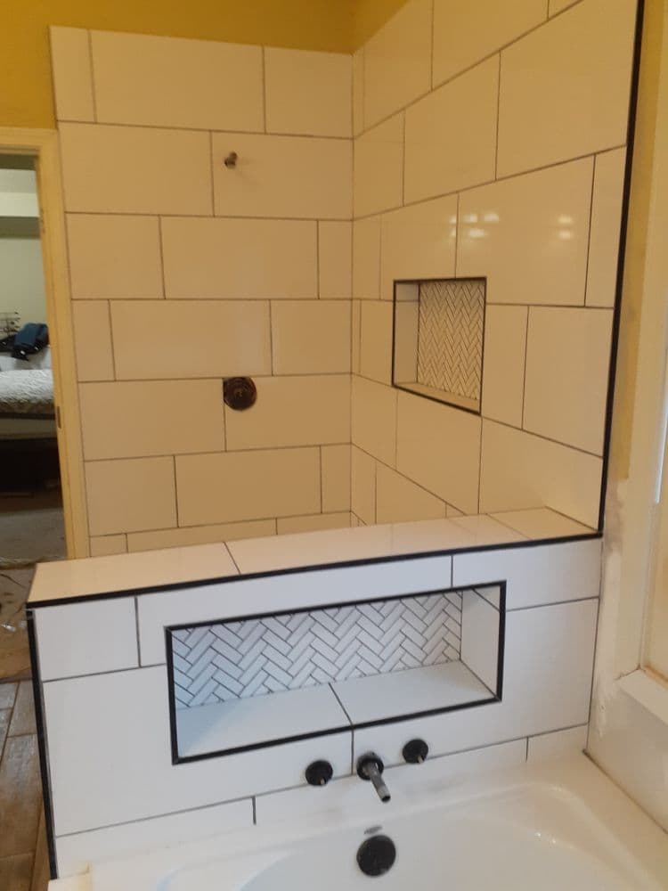 Modern bathroom with white tiled shower, decorative herringbone insert, and tub faucet.