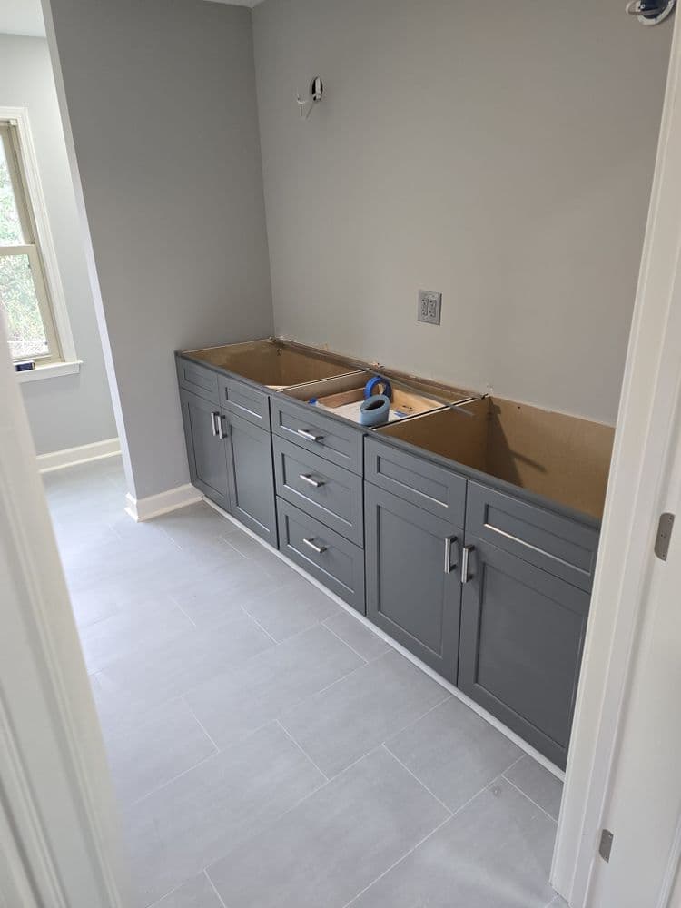 Newly installed gray bathroom cabinets without countertops in a light-colored room.