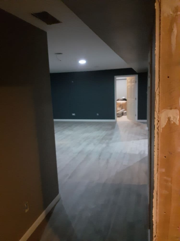 View of a spacious room with gray walls and wood-like flooring, doorway in the background.