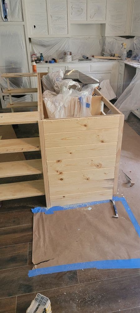 Wooden kitchen renovation in progress with unpacked materials and protective coverings.