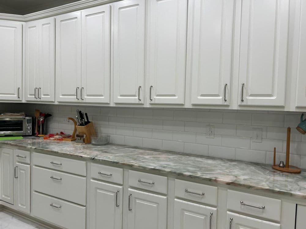 Modern white kitchen cabinets with marble countertop and stainless steel appliances.