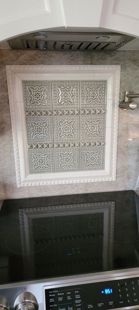 Elegant white kitchen backsplash with intricate gray tile design above modern stovetop.