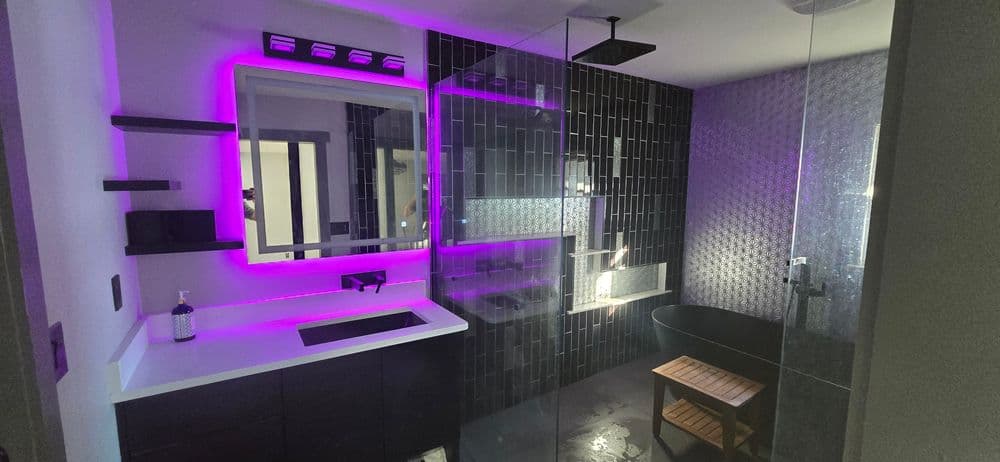 Modern bathroom featuring black tiled walls, illuminated mirror, and sleek walk-in shower.