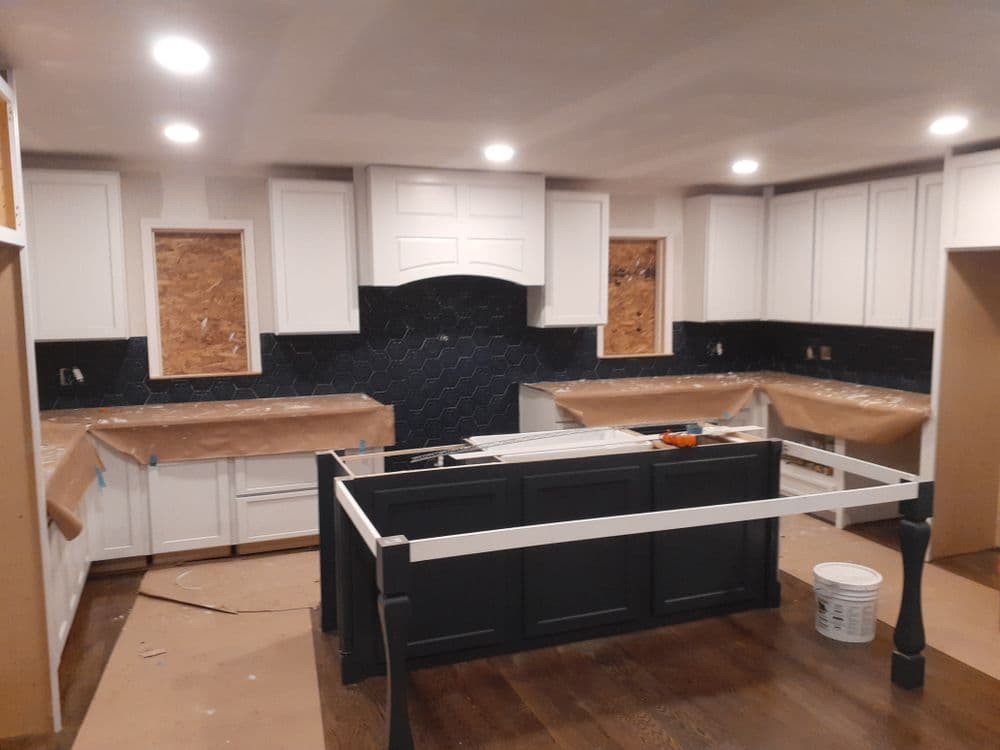 Modern kitchen renovation featuring white cabinetry, dark backsplash, and a central island.