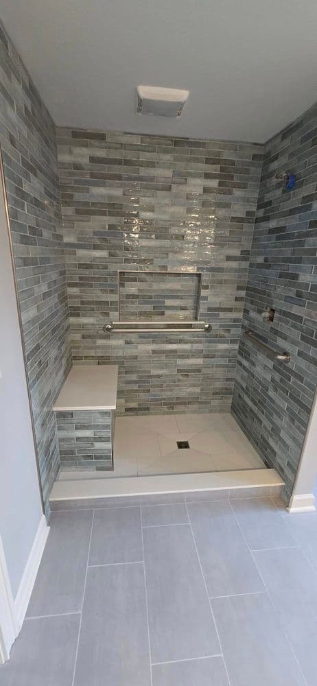 Modern bathroom shower with gray tile walls, grab bars, and sleek accessibility features.