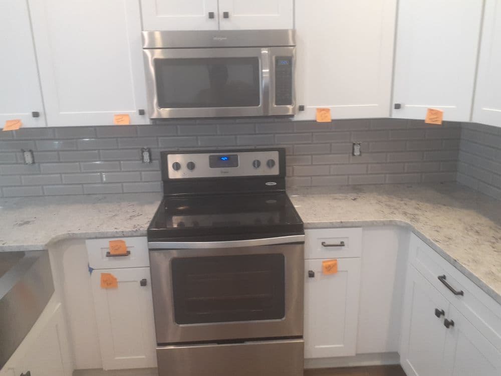 Modern kitchen with stainless steel appliances, white cabinets, and gray tile backsplash.