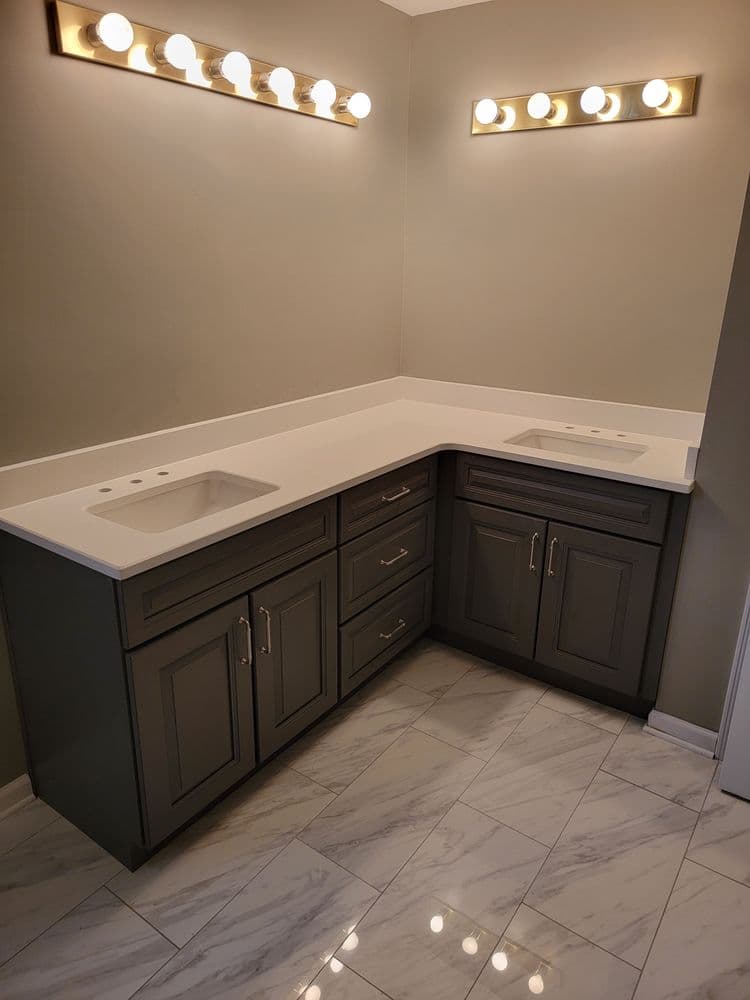 Modern bathroom vanity with double sinks, gray cabinets, and bright lighting. White marble floor.