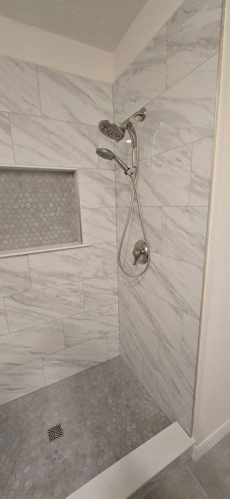 Modern shower with marble tiles, dual showerheads, and pebble stone floor design.