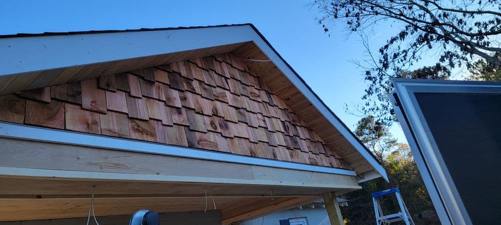 Newly installed wooden roof shingles under a clear blue sky, with construction details visible.