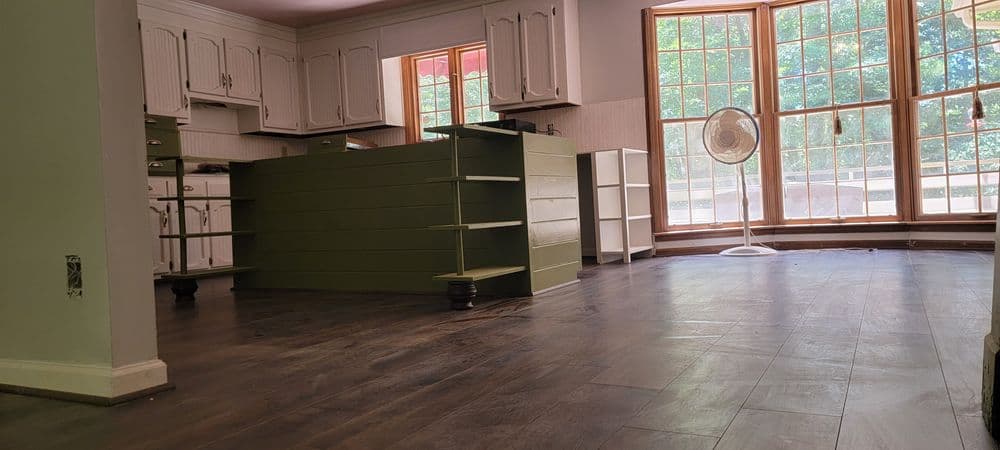 Open kitchen with green island and large windows, featuring hardwood flooring and ample light.