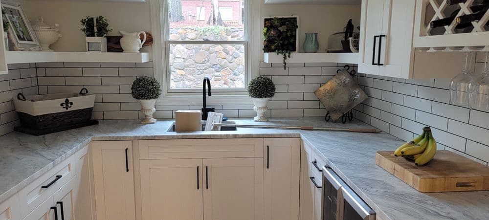 Modern kitchen with white cabinets, marble countertops, decorative plants, and a bowl of bananas.