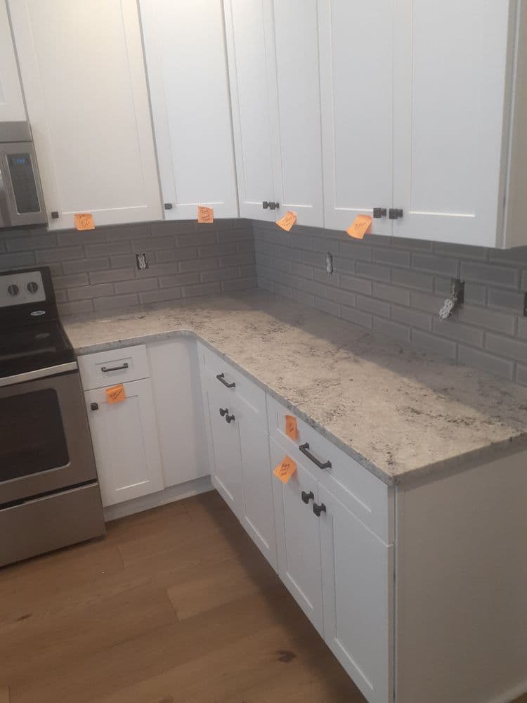 Modern kitchen with white cabinets, gray backsplash tiles, and granite countertop.