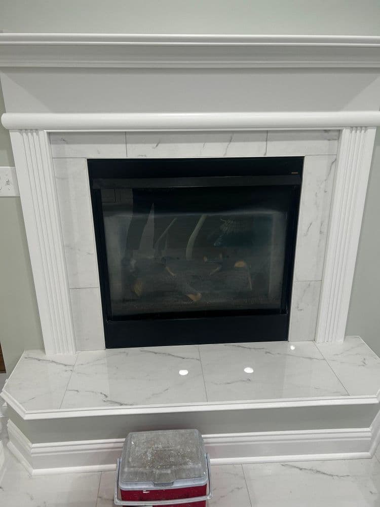 Modern marble fireplace with black insert and sleek mantel against a light wall.