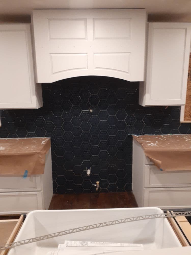 White kitchen cabinets above a dark hexagon tile backsplash with countertops under renovation.