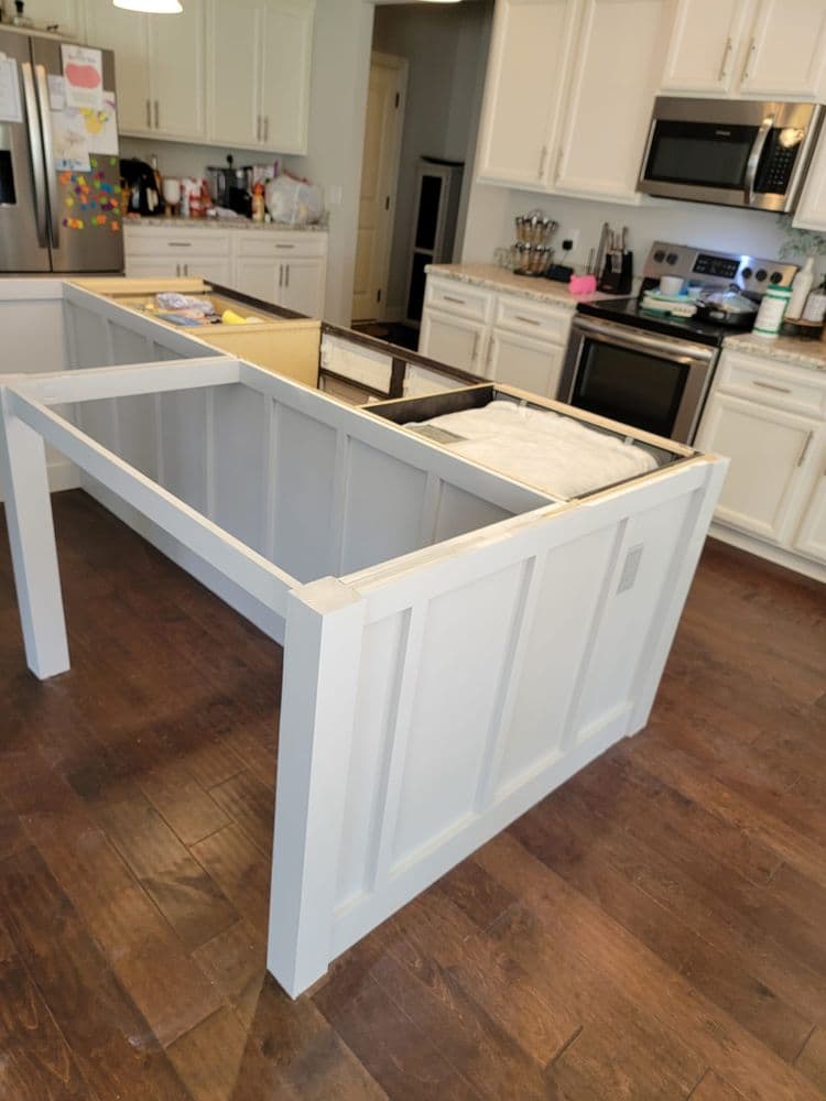 Modern kitchen island under construction with white cabinetry and wooden flooring.