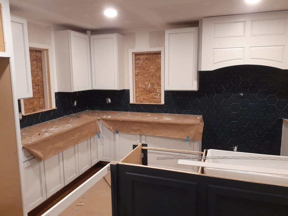 Renovating kitchen with white cabinets, hexagonal backsplash, and uninstalled lower cabinets.