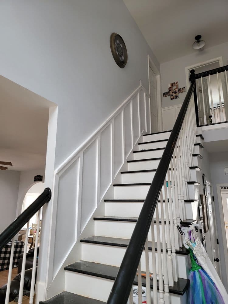 Interior staircase with white walls, black railing, and children's costumes hanging nearby.