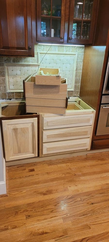 Unfinished kitchen cabinet with stacked cardboard boxes and wooden drawers on wooden floor.