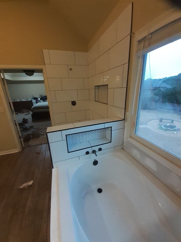 Modern bathroom renovation featuring a white bathtub and tiled shower area with window view.