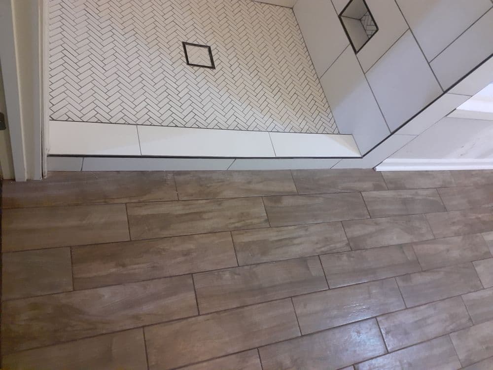 Herringbone tiled shower floor next to wood-look tiled bathroom floor.