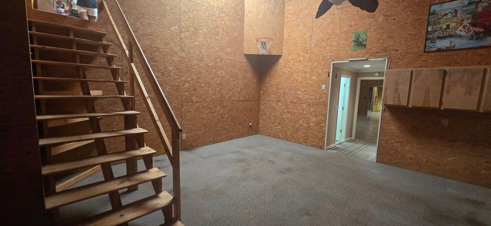 Interior view of a spacious room with wooden stairs, basketball hoop, and storage cabinets.