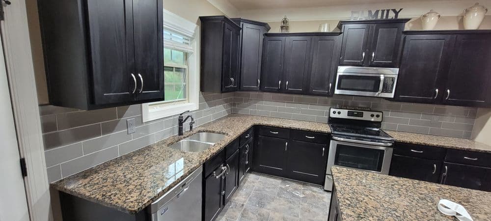 Modern kitchen with dark cabinetry, granite countertops, stainless steel appliances, and gray tile backsplash.