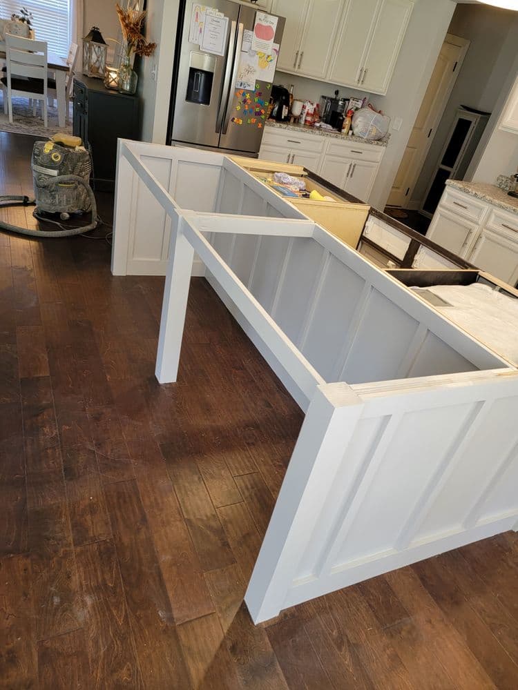Unfinished kitchen island frame in modern kitchen with wooden flooring and appliances.
