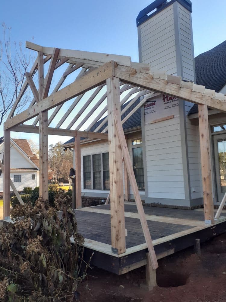 Framing structure of a new porch under construction beside a house with chimney.