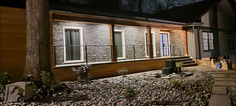Modern home exterior at night with stone accents, porch lights, and landscaped garden.