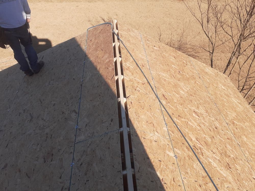 Construction view of a roof apex with framing and safety cables on a sunny day.