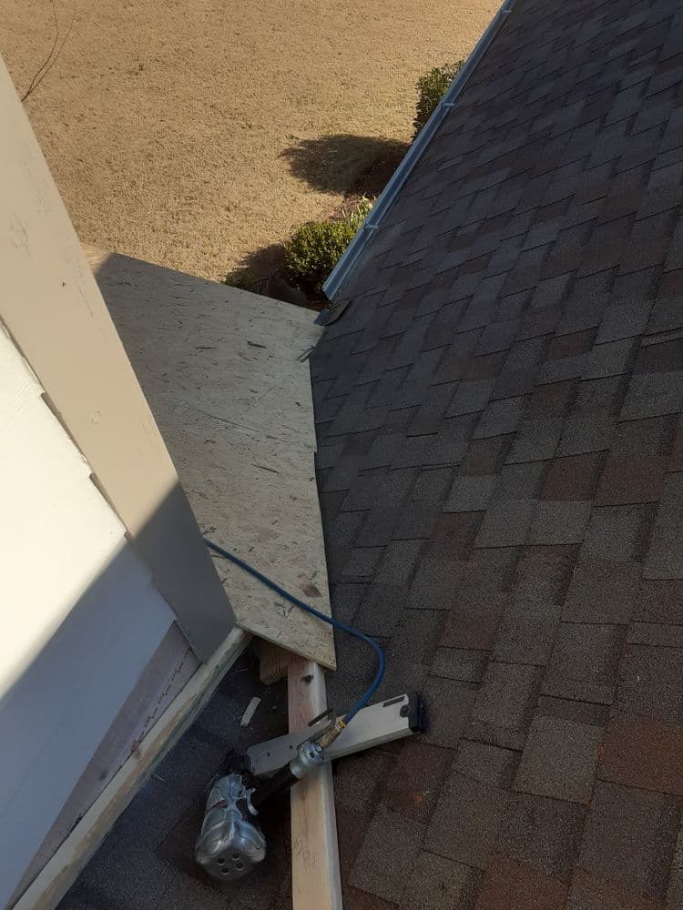 Roofing project showing tools and materials on a sloped surface with brown shingles.