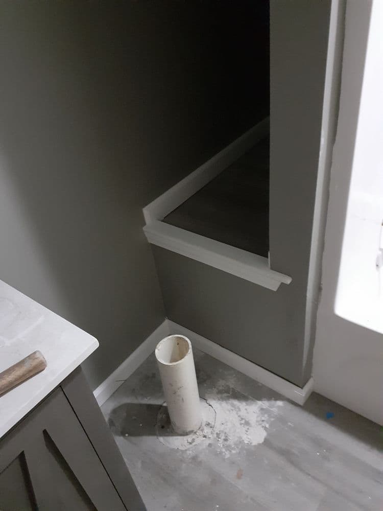 View of a dimly lit hallway with a white pipe and gray walls, showing home renovation progress.